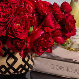 Red rose bouquet in a patterned vase beside a champagne bottle and gift box