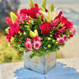 Bouquet of red roses, white lilies, and pink carnations in a square vase