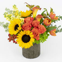 Bouquet of sunflowers, orange roses, and orange tulips in a textured vase