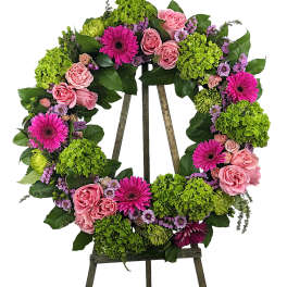 Floral wreath of pink roses, magenta daisies, and green hydrangeas on an easel