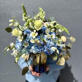 Blue hydrangea bouquet with white roses and snapdragons in a glass vase