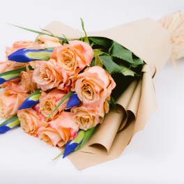 Bouquet of peach roses with blue buds wrapped in tan paper