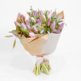 Bouquet of pink and lavender tulips wrapped in tan and white paper