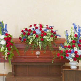Three red, white, and blue floral sprays arranged around a wooden casket