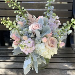 Pastel bouquet of roses, hydrangeas, and tall blue flowers in a glass vase
