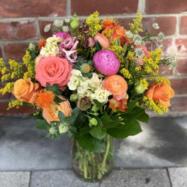 Mixed bouquet of pink, orange, and yellow flowers in a glass vase