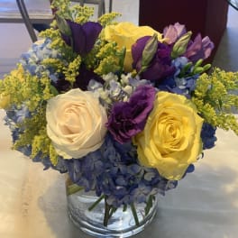 Bouquet of yellow, white, purple, and blue flowers in a clear glass vase