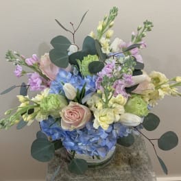 Pastel bouquet with blue hydrangeas, pink roses, and white tulips in a glass vase
