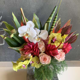 Tropical bouquet with orchids, roses, and red blooms in a glass vase