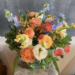 Mixed bouquet of peach, white, and blue flowers in a glass vase