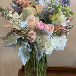 Pastel bouquet of roses, hydrangeas, and blue flowers in a glass vase
