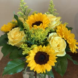 Yellow sunflowers and roses arranged in a clear glass vase