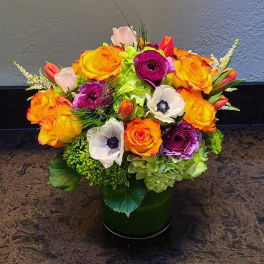 Bouquet of orange and purple roses with white anemones in a green vase