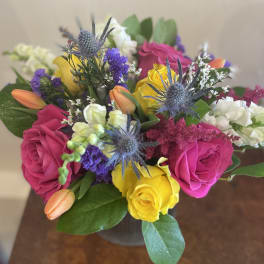 Bouquet of pink and yellow roses with purple thistle in a vase
