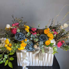 Colorful floral arrangement in a white pleated container with blue and yellow blooms