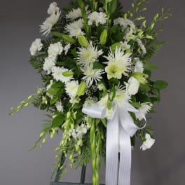 White floral standing spray with a white ribbon on an easel