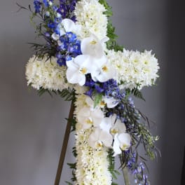 White floral cross arrangement with blue flowers on an easel