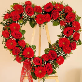 Heart-shaped floral wreath with red roses and gerbera daisies on an easel