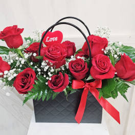 Red roses in a black gift bag with a red heart pick