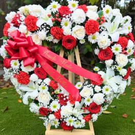 Heart-shaped floral wreath with red and white flowers and a pink ribbon