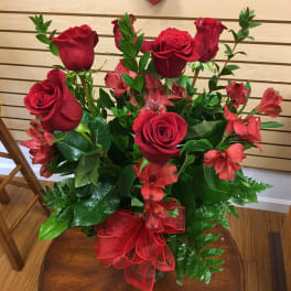 Red roses and red alstroemeria in a glass vase with a red ribbon
