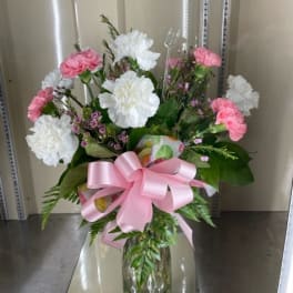 Pink and white carnations in a glass vase with a pink ribbon