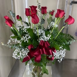 Red roses in a clear glass vase with white baby's breath and a burgundy ribbon