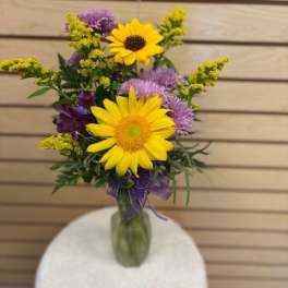 Bouquet of yellow sunflowers and purple flowers in a glass vase
