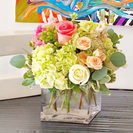 Bouquet of pink and peach roses with pale green hydrangeas in a clear glass vase