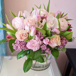 Pink and white bouquet of roses, tulips, and orchids in a glass vase