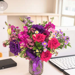 Bright mixed bouquet of pink, purple, and white flowers in a glass vase