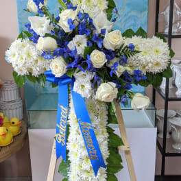 White and blue funeral standing spray on an easel with ribbon streamers