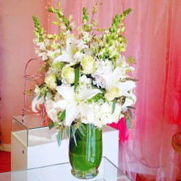 Tall white floral arrangement in a green glass vase