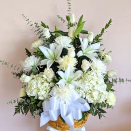 White floral arrangement in a woven basket with a large white ribbon