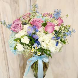 Pink roses and blue flowers in a glass vase with a blue ribbon
