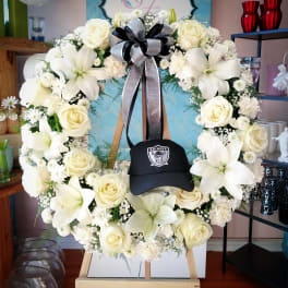 White floral wreath on an easel with a black Raiders cap in the center