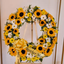 Standing round wreath of yellow sunflowers and white daisies with a yellow bow on an easel