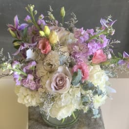 Pastel bouquet with roses, hydrangeas, and purple blooms in a glass vase
