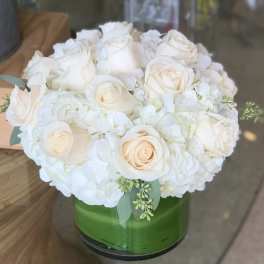White roses and hydrangeas arranged in a green glass vase