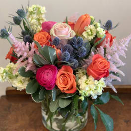 Mixed bouquet of roses, tulips, and purple thistle in a glass vase