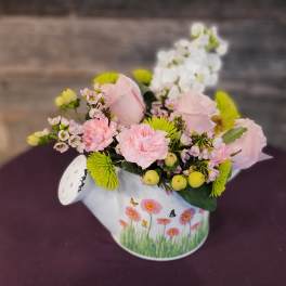 Low arrangement of pink roses and carnations with white blooms in a painted watering can.