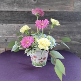 Pink gerbera daisies and pale yellow carnations in a small decorative pot