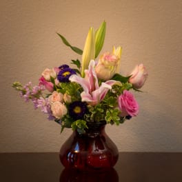 Mixed bouquet of lilies, roses, and purple daisies in a red glass vase