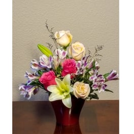 Mixed arrangement of pink and cream roses, lilies, and purple alstroemeria in a red vase