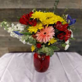 Mixed bouquet in a red glass vase with yellow, red, white, and pink flowers