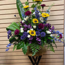 Tall mixed flower arrangement in a bronze vase with yellow, purple, blue, and white blooms