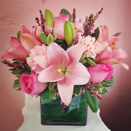 Pink lilies and roses arranged in a square glass vase