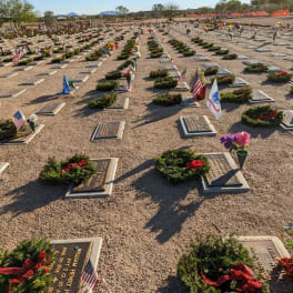 Rows of grave markers with wreaths, flowers, and small flags in a cemetery