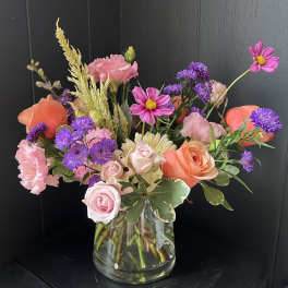 Mixed pink, purple, and orange flowers in a clear glass vase.