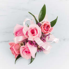 Pink rose corsage with purple filler flowers and pink ribbon on a white surface